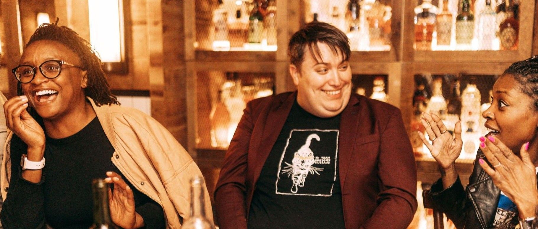 three diverse people laughing and having conversation while sitting around a dinner table at a public setting restaurant