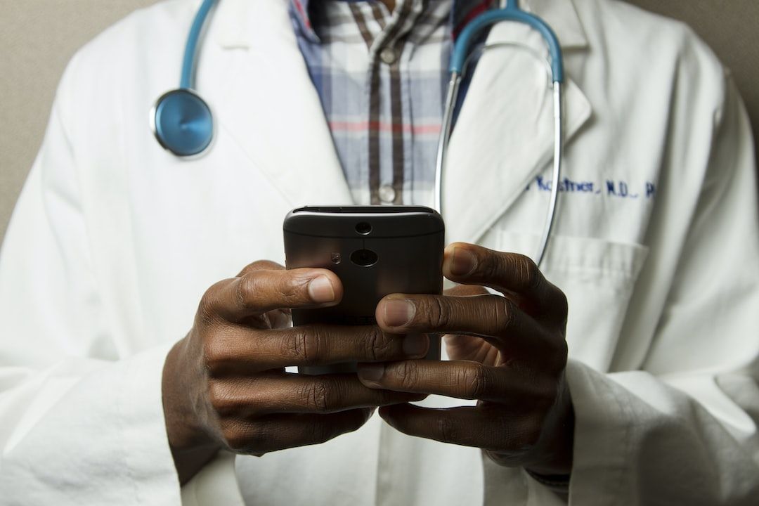 Close up of a doctor's torso with the doctor having a stethoscope around their neck and holding a mobile device