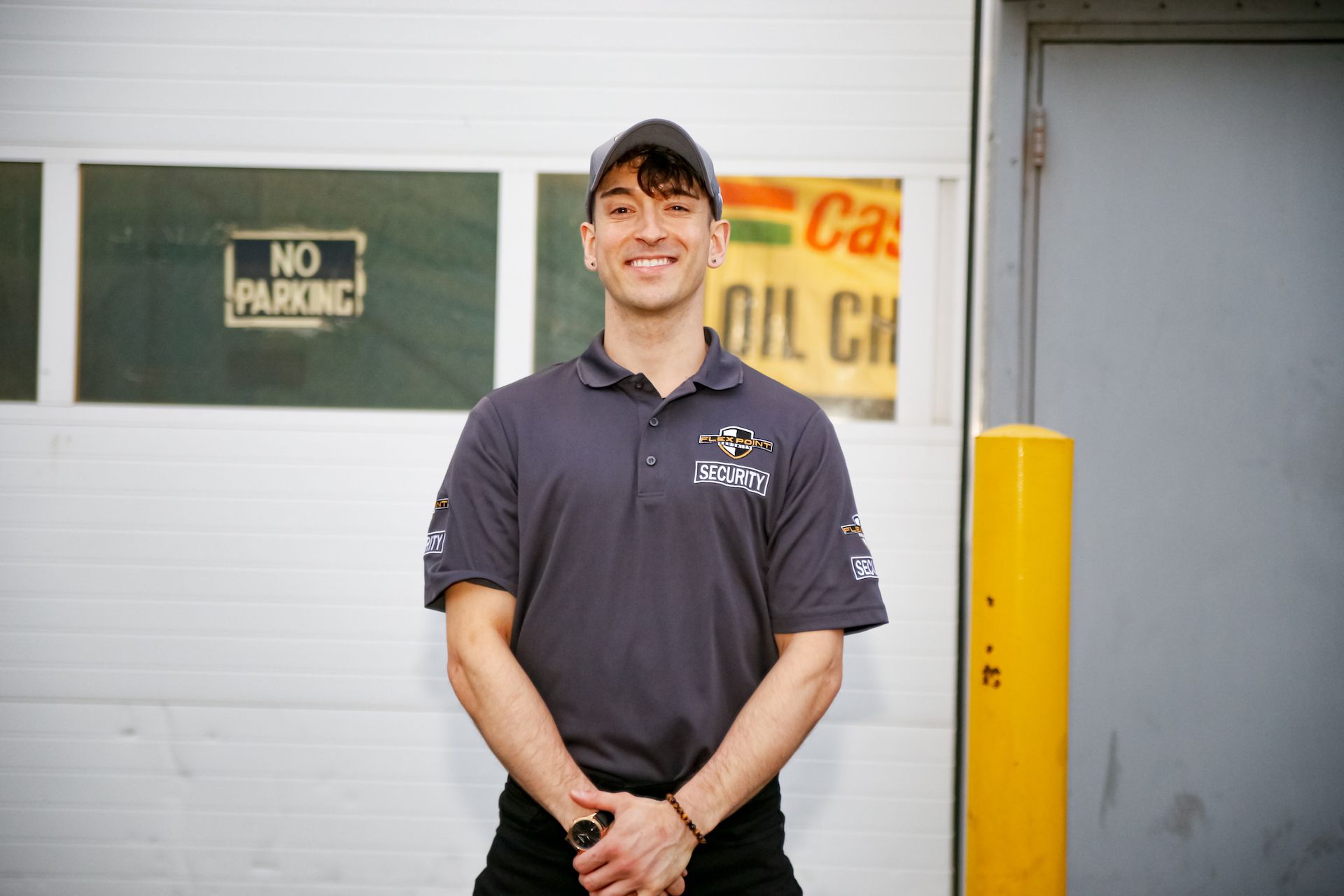 A male Flex Point Security guard smiling as he stands outside of a client's site next to a door and yellow pole