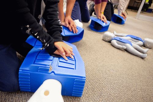 Two females in Flex Point Academy's first aid & CPR training smiling as they get trained using a blue dummy / mannequin 