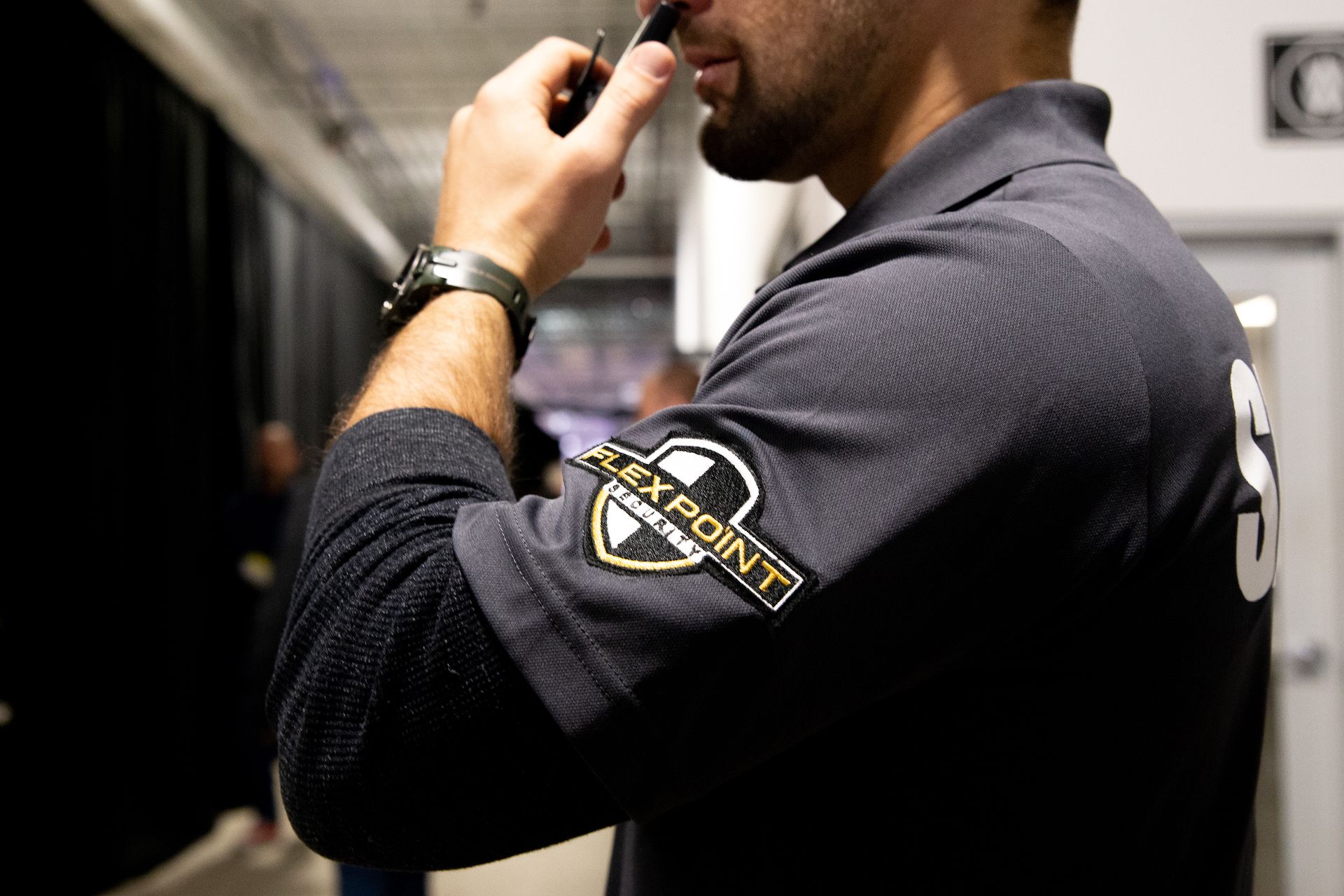 A male Flex Point Security guard at an event using a walkie talkie to communicate with other guards about a major incident