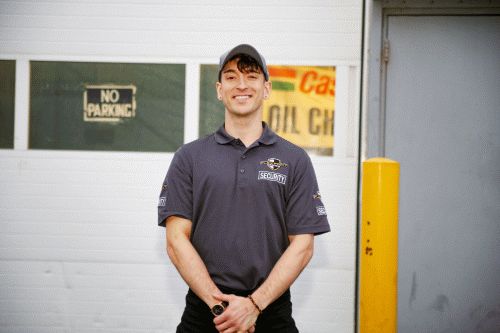 A male Flex Point Security guard smiling as he stands outside of a client's site next to a door and yellow pole