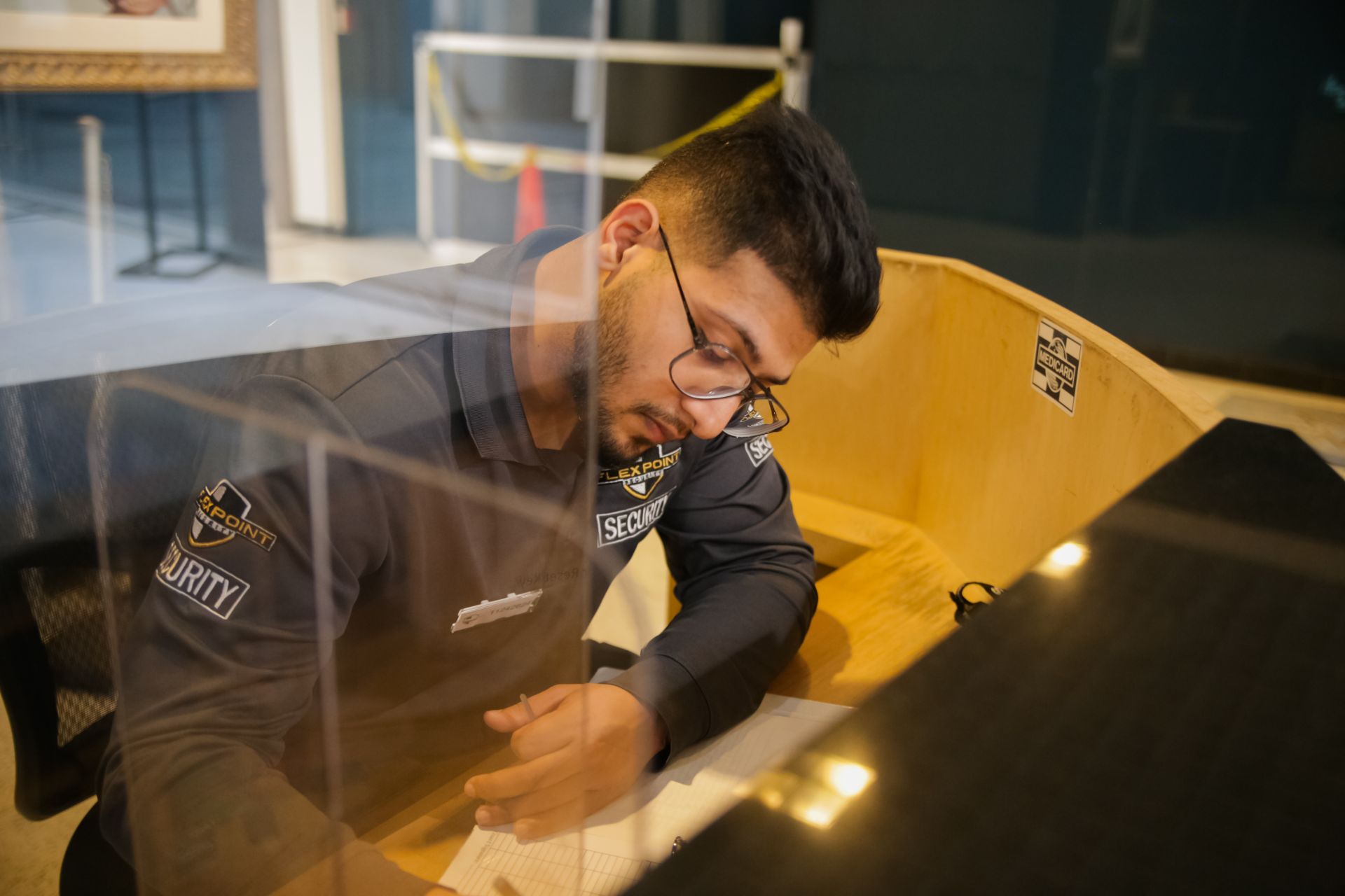 A male Flex Point Security guard seated at a desk in a client's building writing a security report