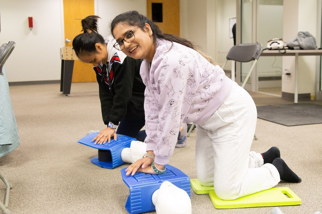 Two females in Flex Point Academy's first aid & CPR training smiling as they get trained using a blue dummy / mannequin 