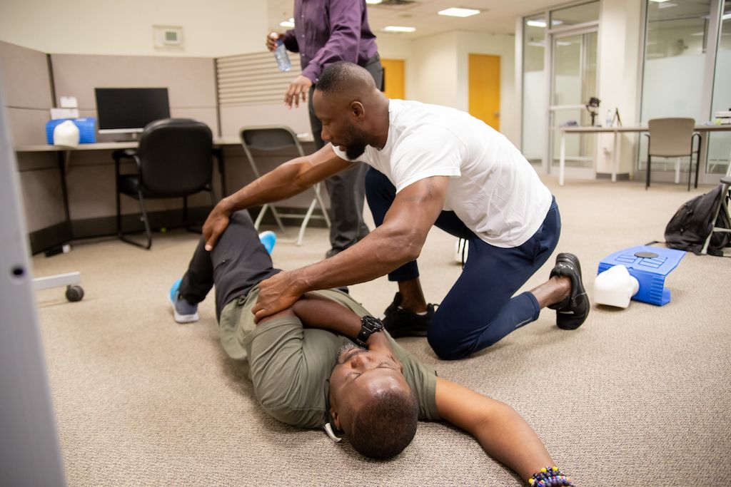 Two trainees being taught by a Flex Point Academy instructor how to do CPR with one trainee lying on the ground and the other practicing the techniques
