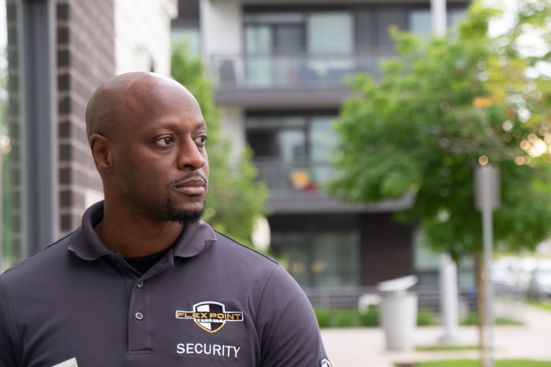 A male Flex Point Security guard standing outside of a residential complex building that he is patrolling