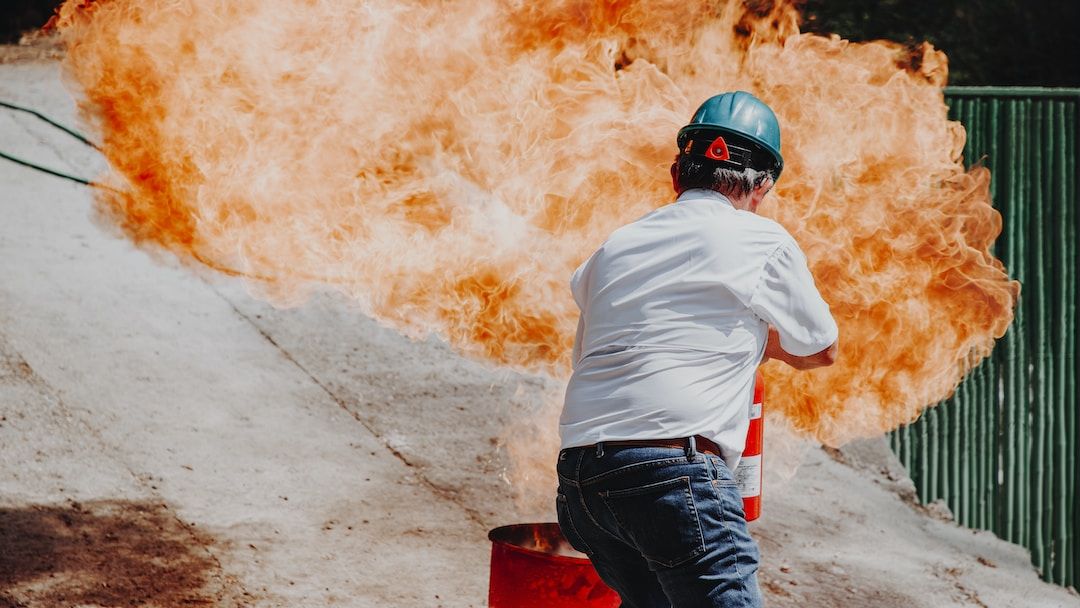 A male with a construction hat on using a fire extinguisher to put out a massive fire