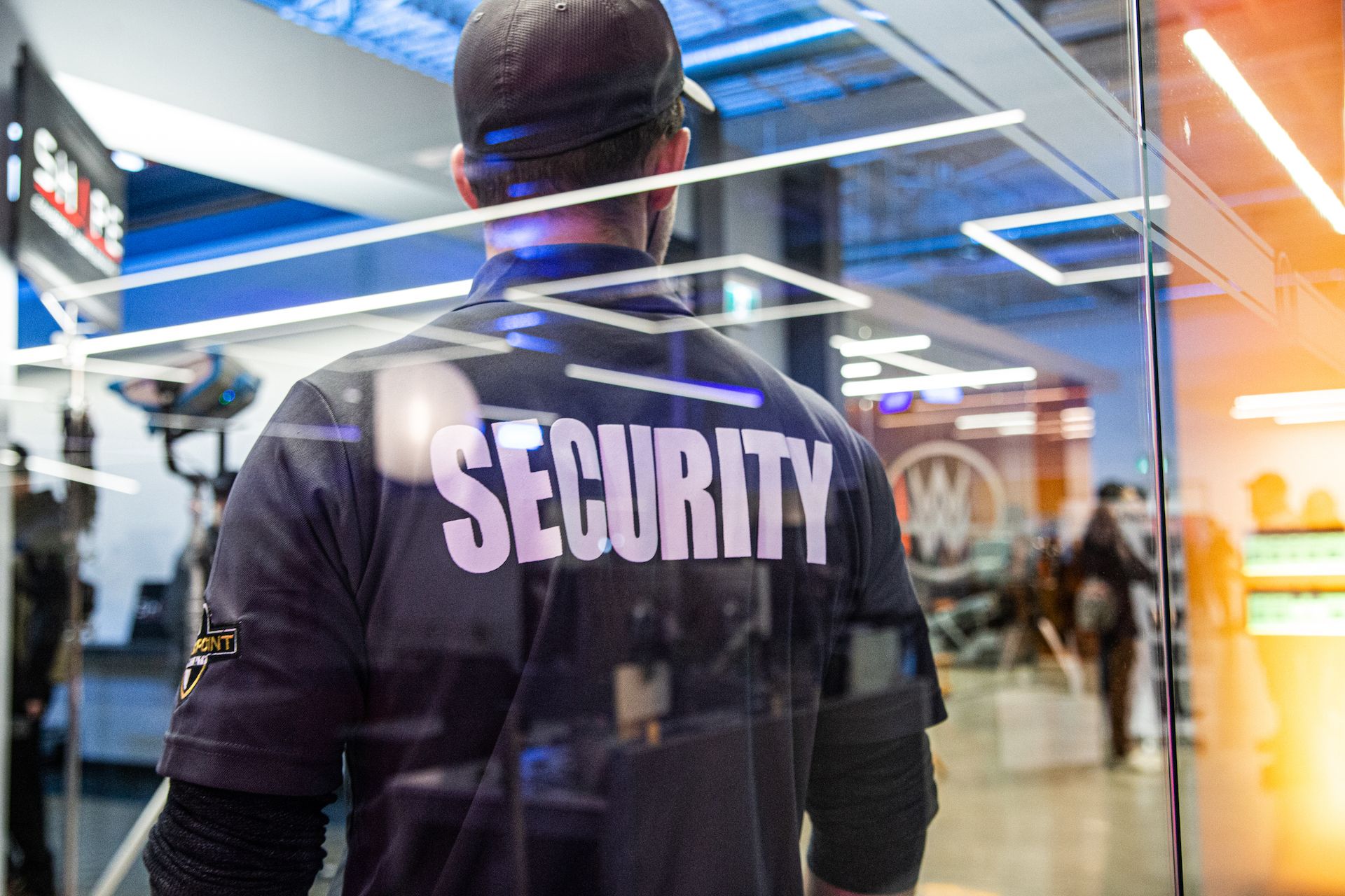 The back of a male Flex Point Security guard with "security" written in large print on the back of his shirt while he monitors activity at an event