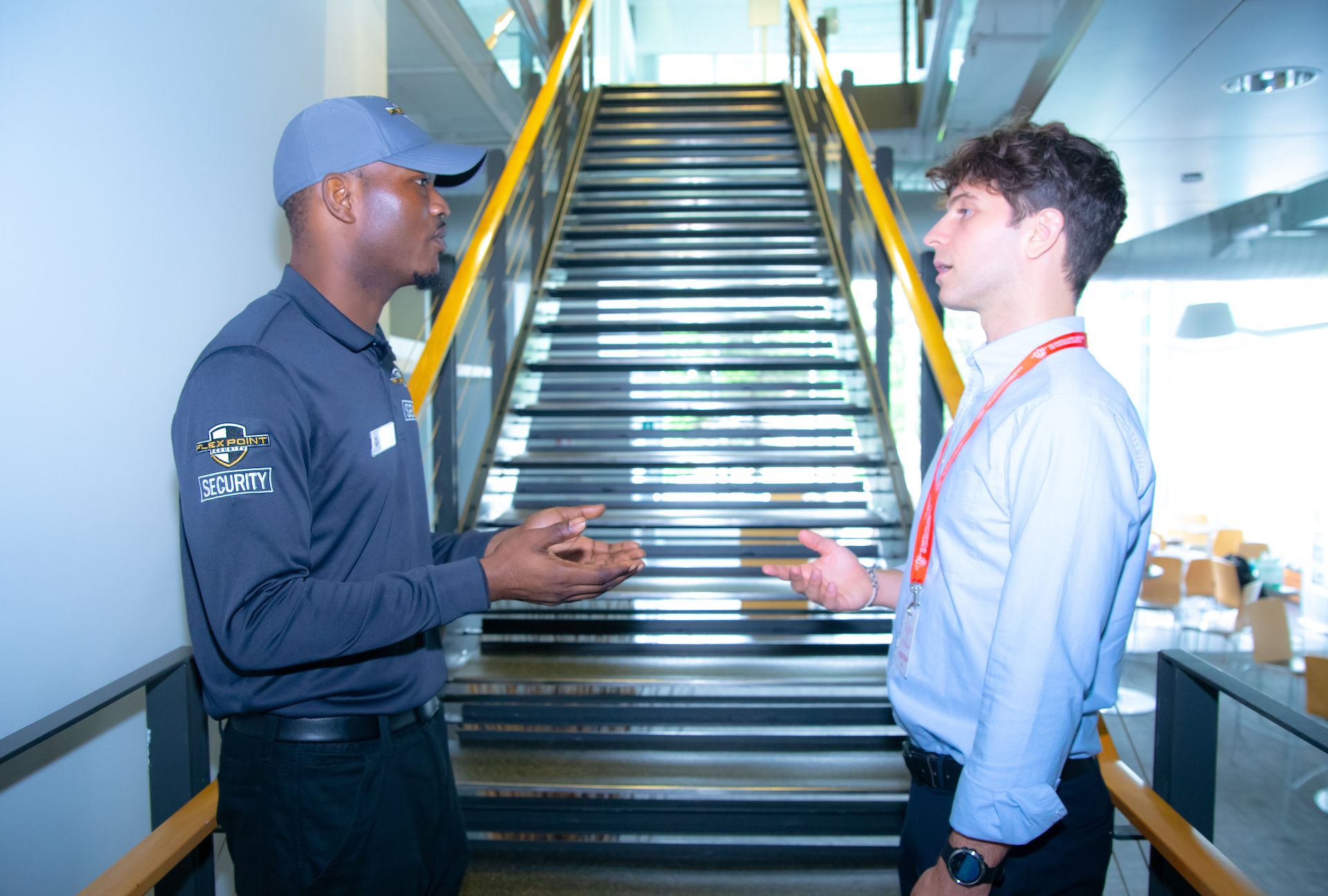 A male Flex Point Security guard interacting with an employee next to a set of stairs in a corporate office