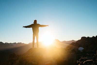 Man standing on cliff in front of sunburst