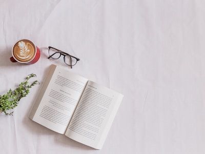 Open book next to pair of glasses and coffee