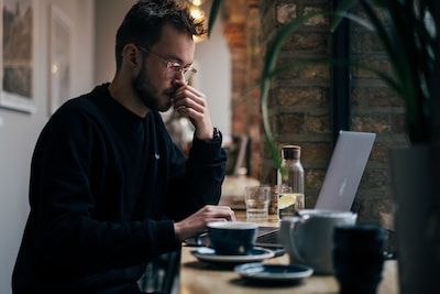 Man thinking sitting at laptop drinking coffee