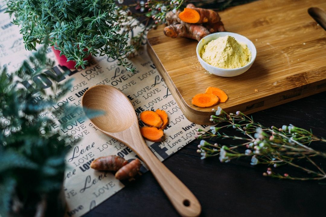 A dark kitchen counter is shown with some wrapping paper that reads ‘love’, a cutting board with a yellow-white powder, some turmeric cuttings, a wooden spoon, and tree and bush foliage.