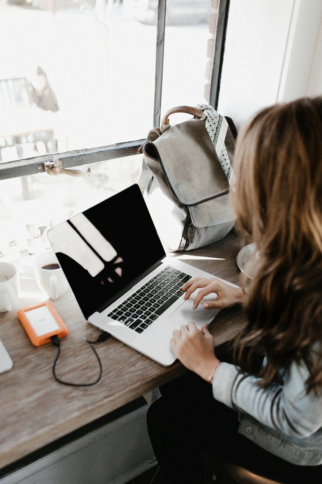 A woman sits on the ground in front of her laptop with her legs crossed. She has her left hand on the opposite knee in a stretch. She has curly hair and sits in front of a green plant. There are candles lit around her.