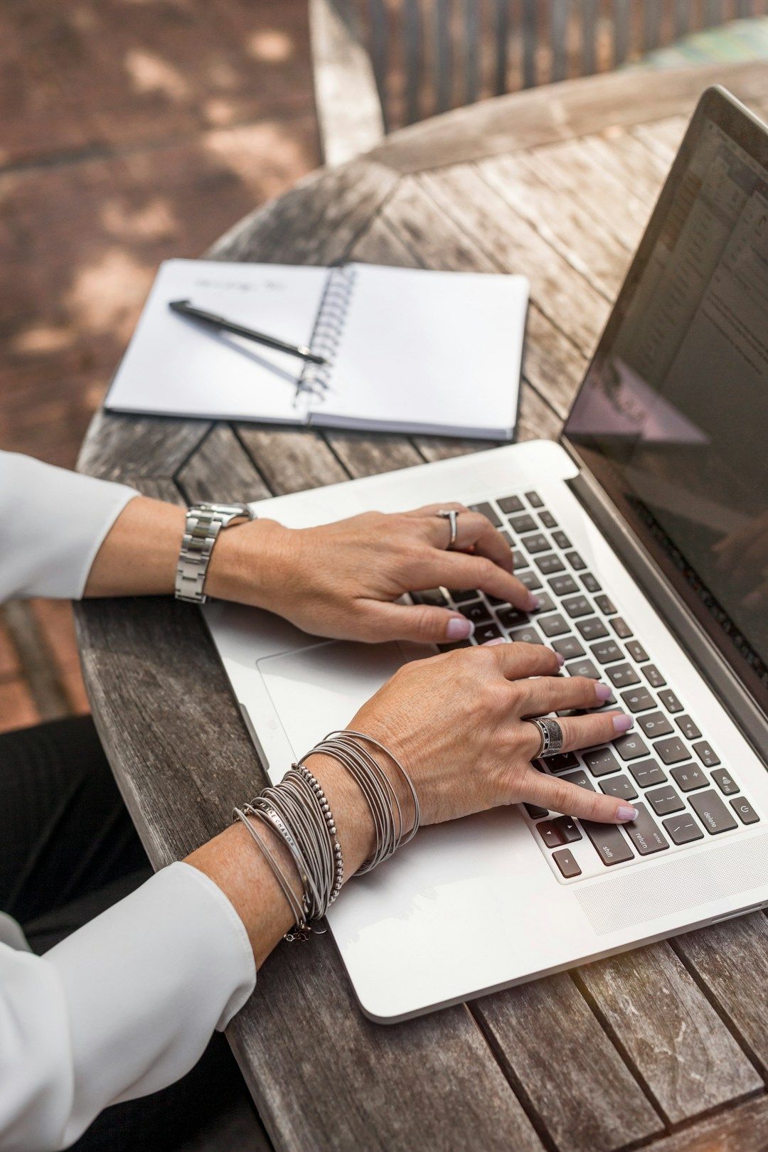 A woman sits on the ground in front of her laptop with her legs crossed. She has her left hand on the opposite knee in a stretch. She has curly hair and sits in front of a green plant. There are candles lit around her.