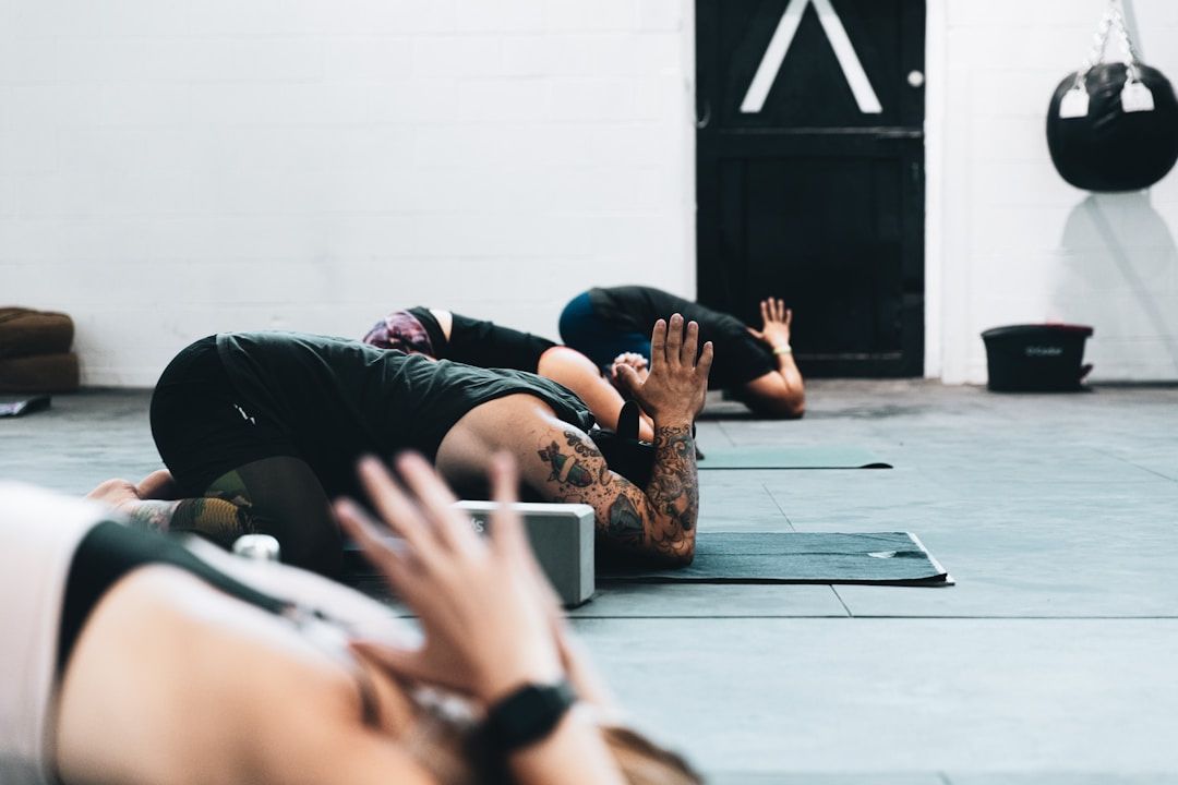 A group of yoga practitioners are all in child's pose. They are in a room with gray flooring and white washed walls.
