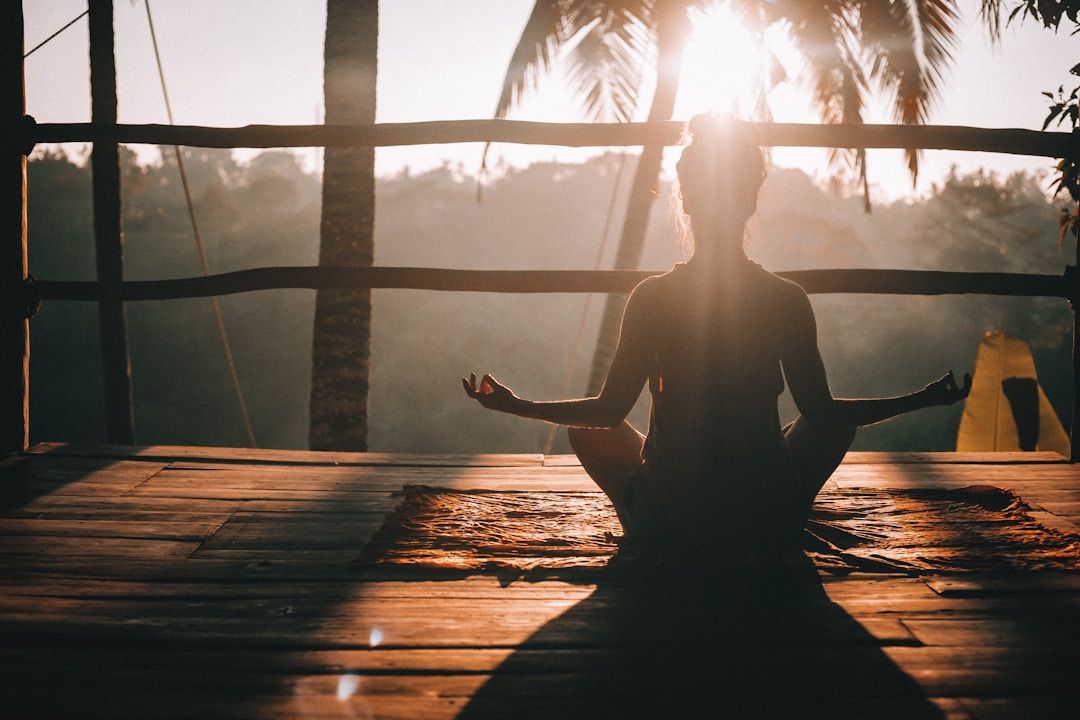 A woman sits on a hidden deck with a rough roof structure during golden hour, drenched in orange sunset light. In front of the deck a lush forest is visible. 