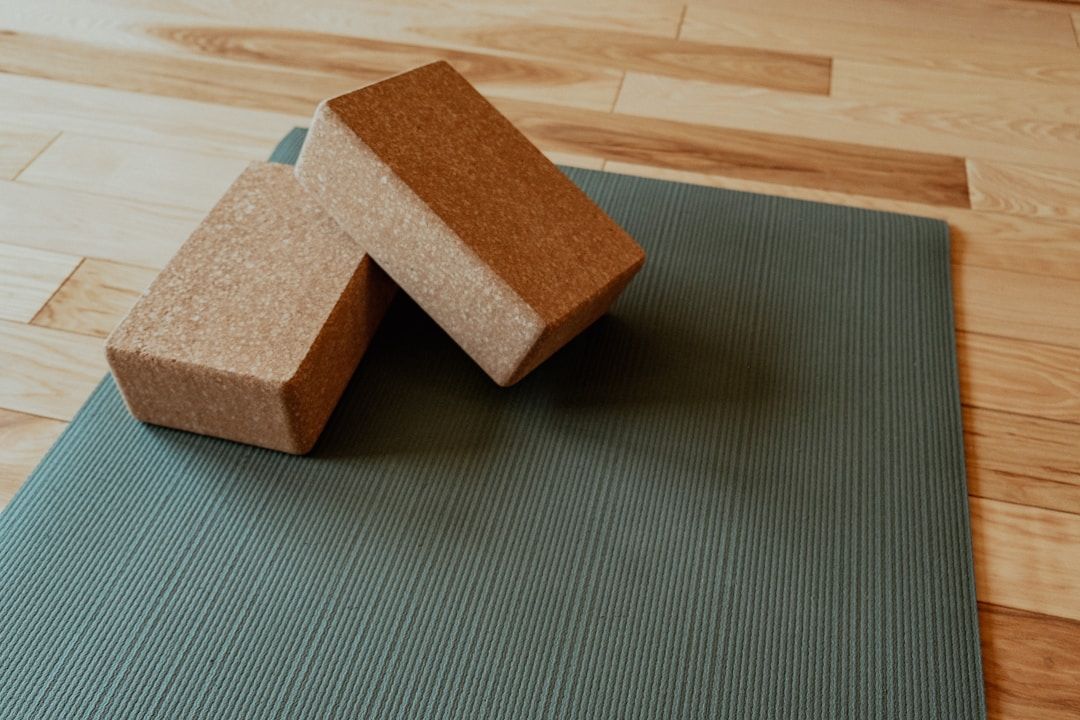 A dark-green yoga mat is shown on a wooden floor with two cork blocks on top. 