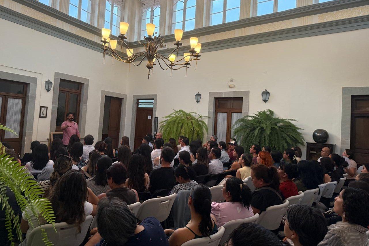 Una sala con candelabro, llena de personas que escuchan una conferencia.