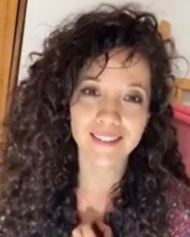 Retrato de Carolina Muñoz Aliaga, sonriente, con el pelo rizado suelto.