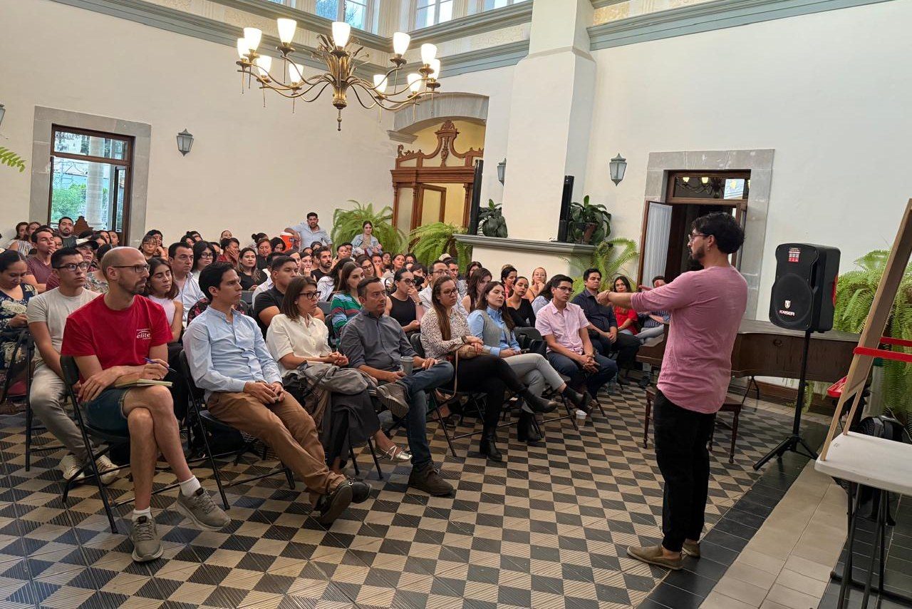 Andrés Esteban Cárdenas, de pie, explica con un gesto ante un público adulto sentado.