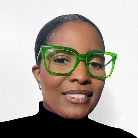 A Black woman with her fair slicked back, wearing vibrant green glasses and smiling at the camera