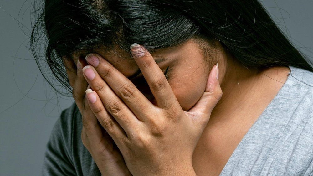 A Brown woman cries into her hands