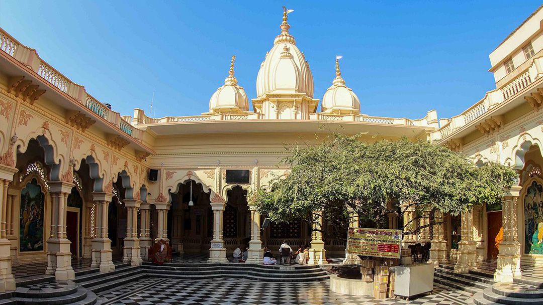A white Vaishnava temple with carved domes and a chequered marble courtyard
