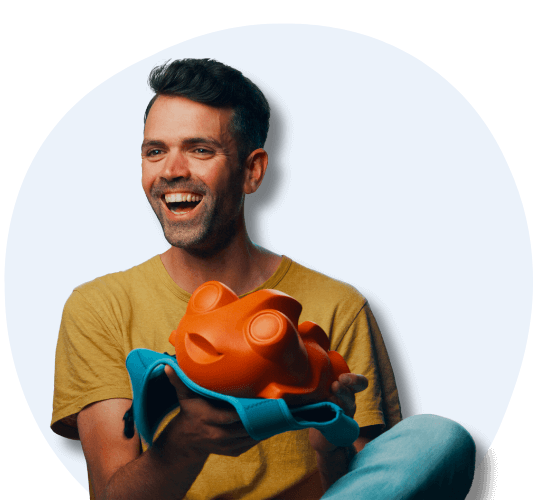 A smiling man holding an orange, frog shape floaty designed for children.