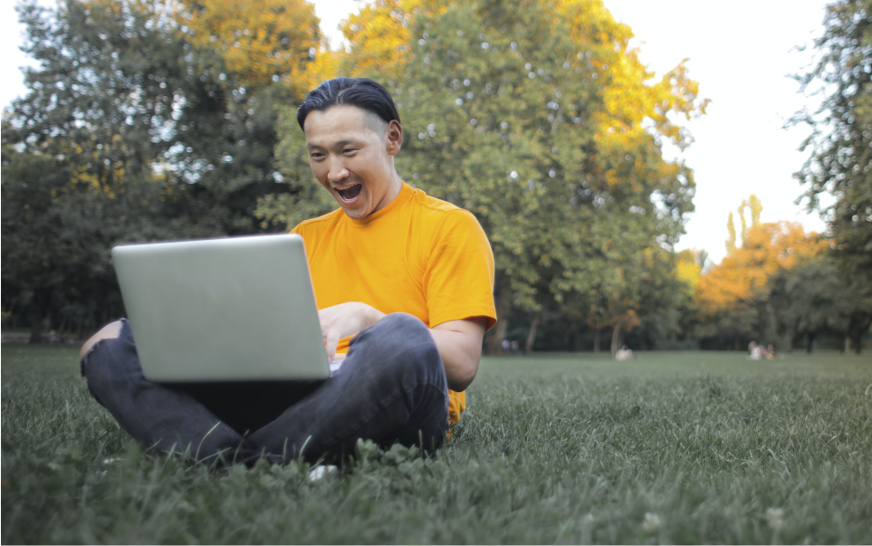 Tester de software feliz en un parque  con su laptop en las piernas