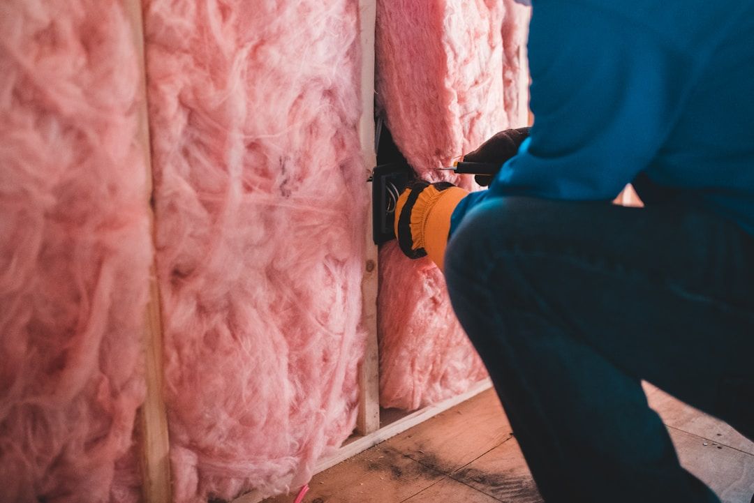  A person installing pink fiberglass insulation batting into a wall cavity. 