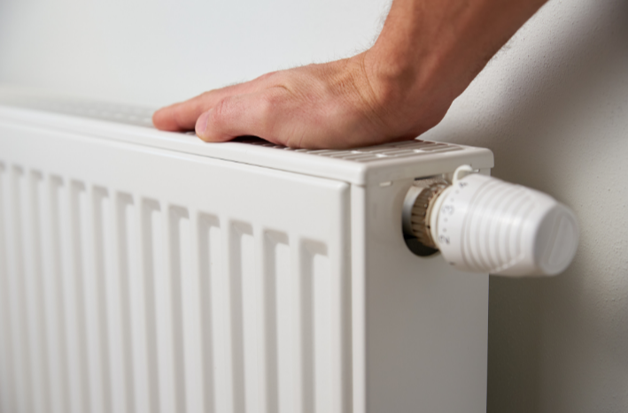 Main vérifiant la température d'un radiateur blanc, système de chauffage central résidentiel aux normes québécoises RBQ 15.4.1 