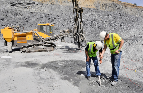 Boutefeux professionnels préparant tir de mines : experts en explosifs avec EPI réglementaires sur carrière, foreuse visible