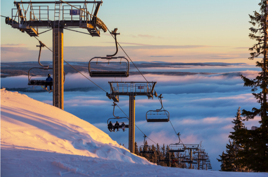 Remontée mécanique au coucher du soleil dans une station de ski, télésièges surplombant une mer de nuages avec neige fraîche au premier plan RBQ 1.10