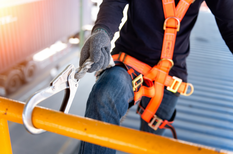 Construction worker wearing orange safety harness with fall protection equipment on high-rise building site following Canadian safety regulations