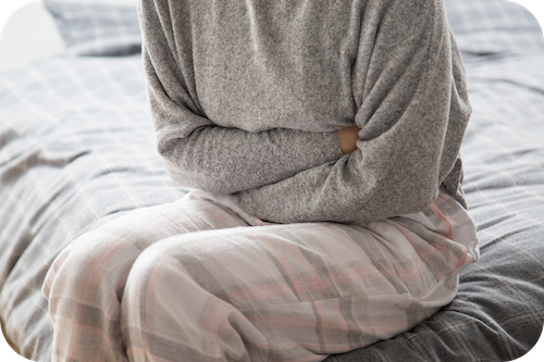 Person sitzt mit verschränkten Armen auf dem Bett