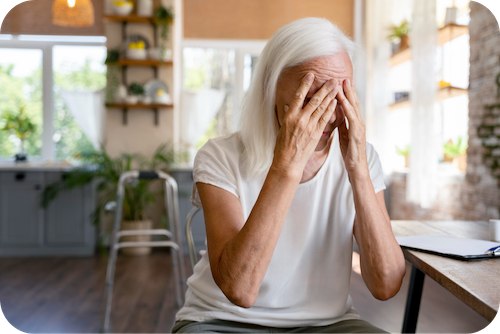 Ältere Dame mit grauen Haaren schlägt die Hände vor das Gesicht und weint