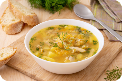 Eine warme Suppe steht auf einem Brett mit Löffel daneben