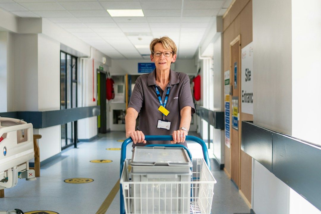 Eine ältere Mitarbeiterin schiebt einen Wagen durch einen Krankenhaustrakt.