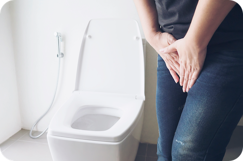 Person steht neben Toilette und fasst sich an den Schritt