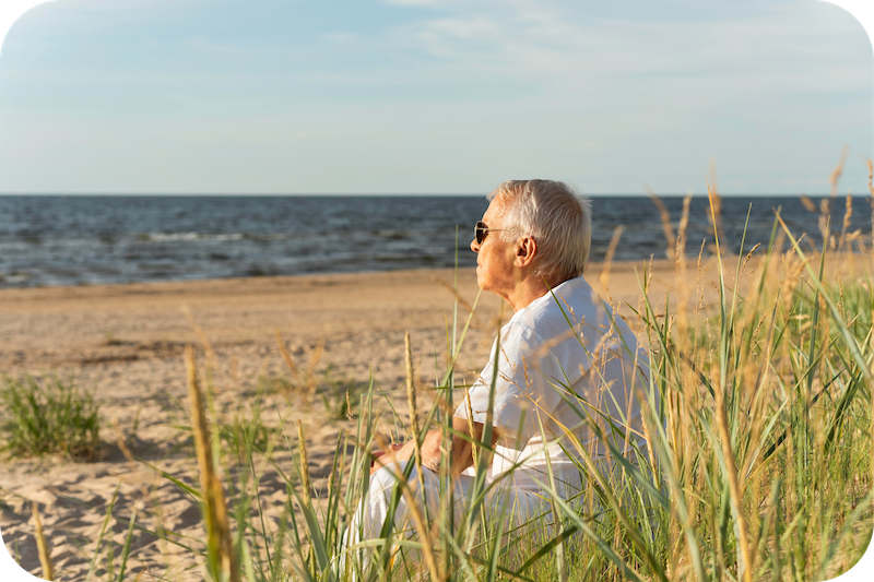 Älterer Herr sitzt am Strand an der Nordsee und genießt die Sonne