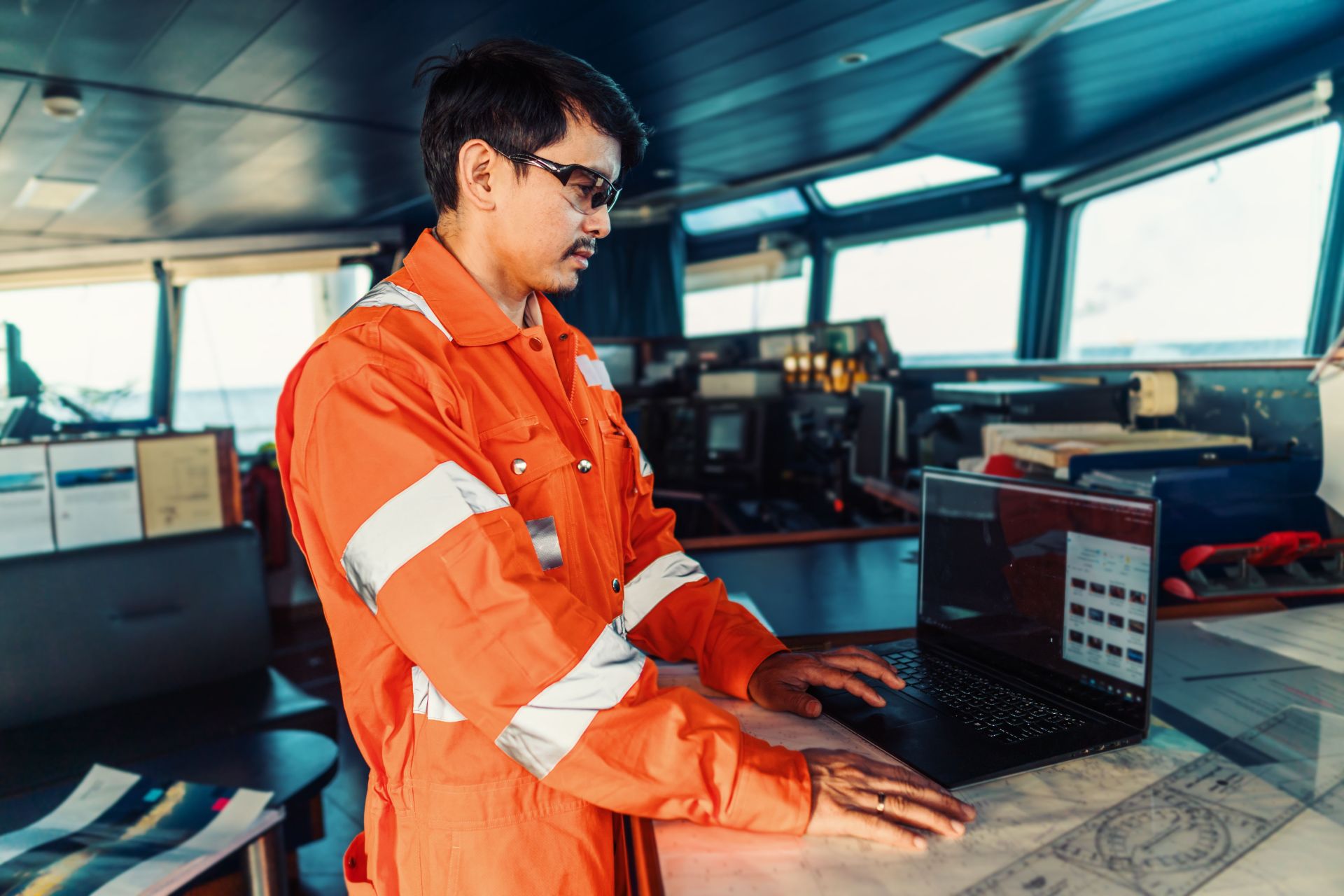Navigational officer analyzing data on laptop aboard ship's bridge, showcasing maritime technology integration in modern vessel management.
