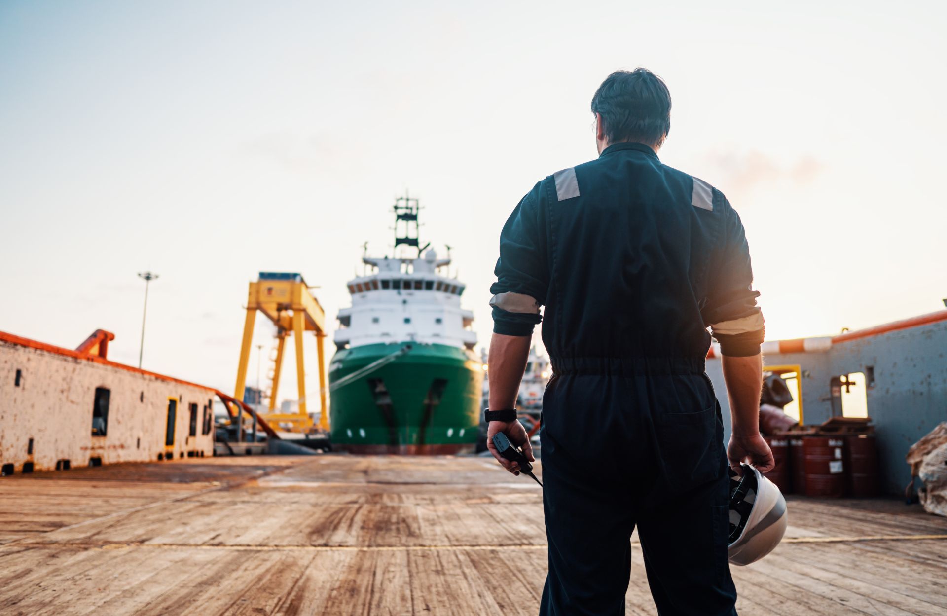 Maritime professional overlooking a cargo ship at the harbor during sunset, symbolizing industry expertise and leadership in maritime training and safety.