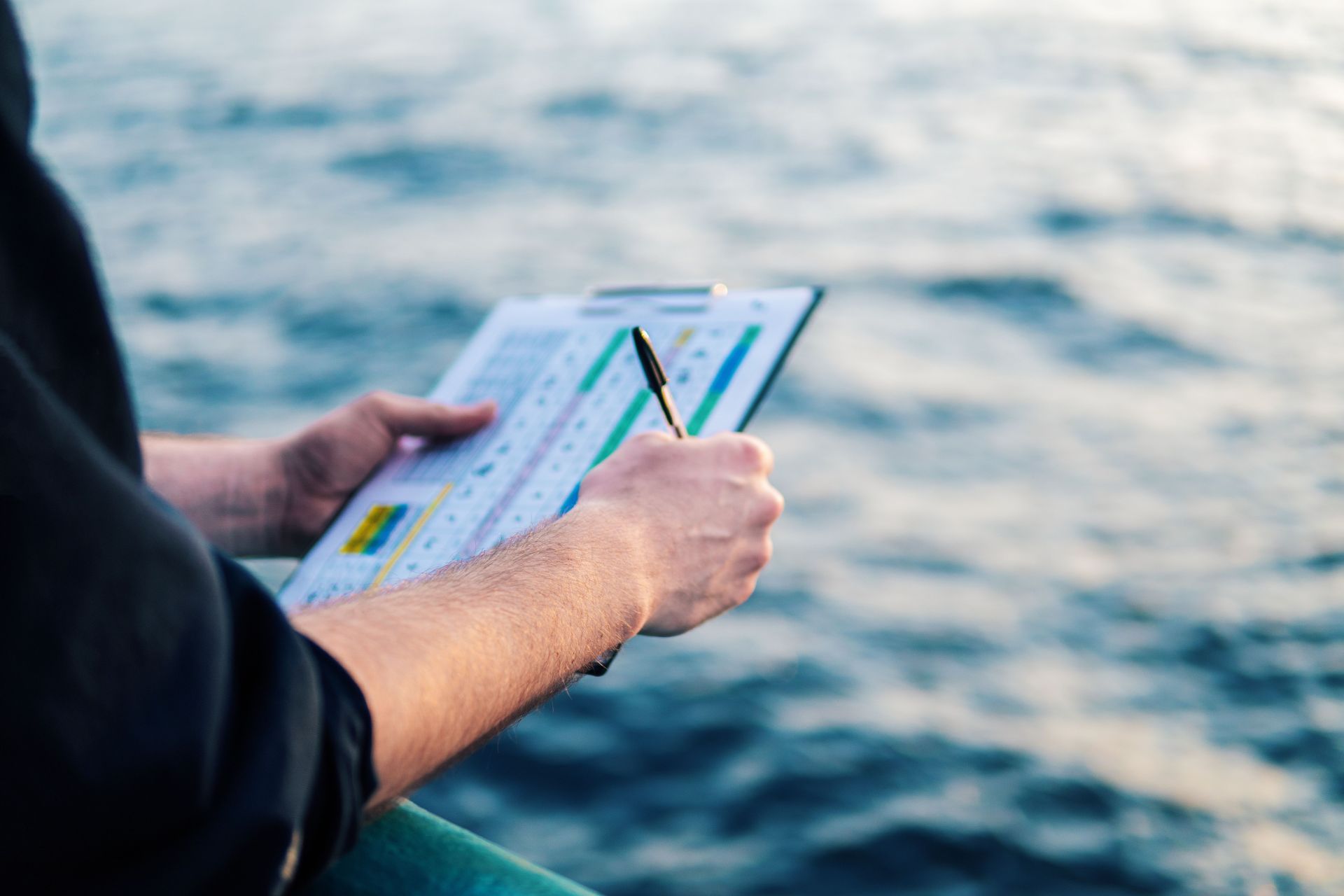 Close-up of a mariner's hands using a navigation chart and dividers on the deck of a ship.
