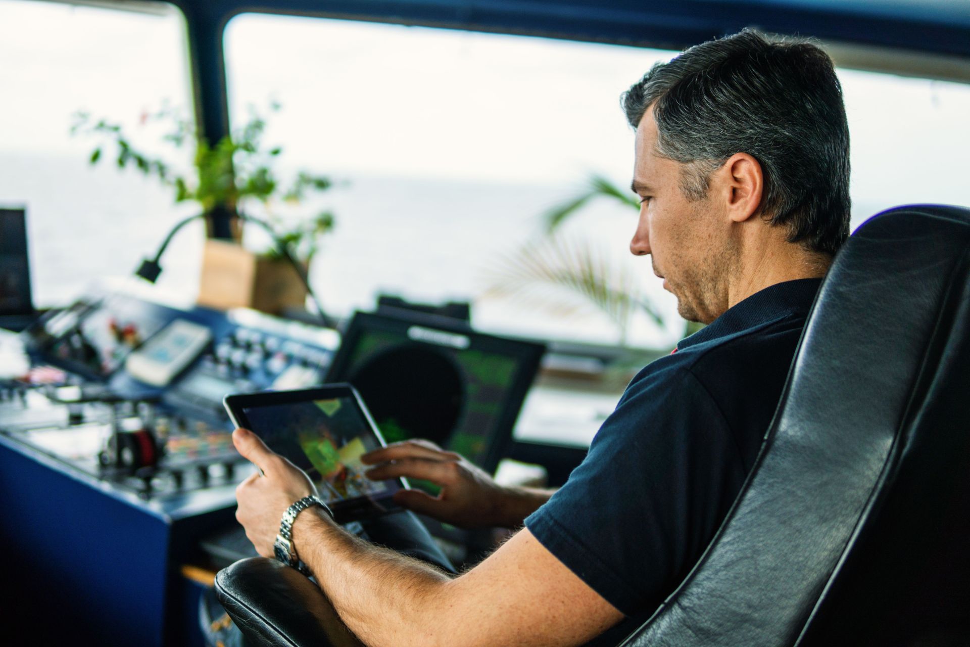 Experienced maritime navigator using a digital tablet in the ship's control room with ocean views.