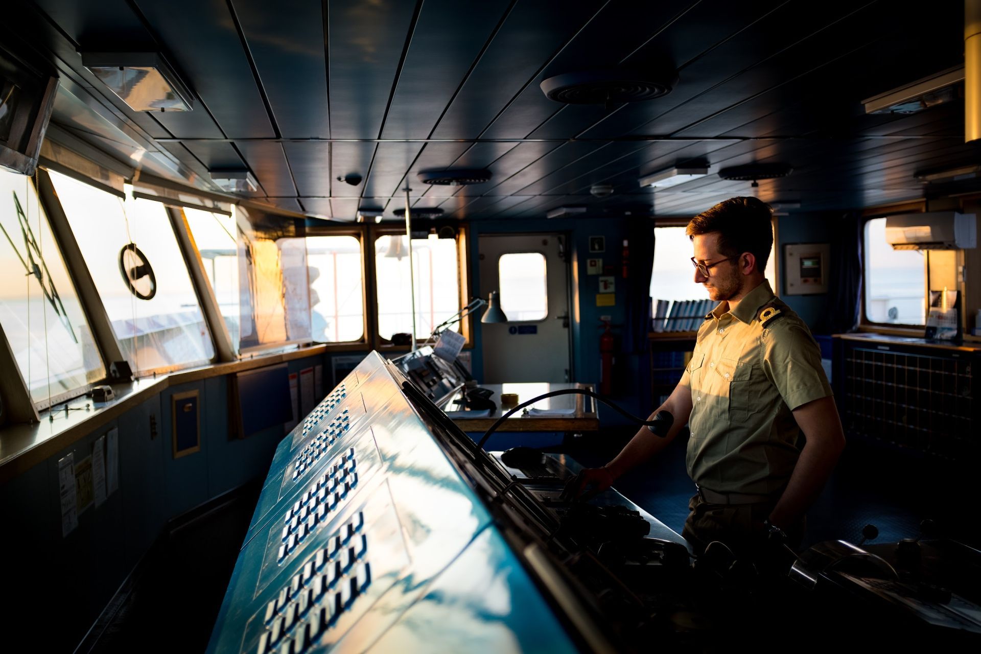 Ship officer operating navigational equipment in the bridge of a vessel during golden hour.