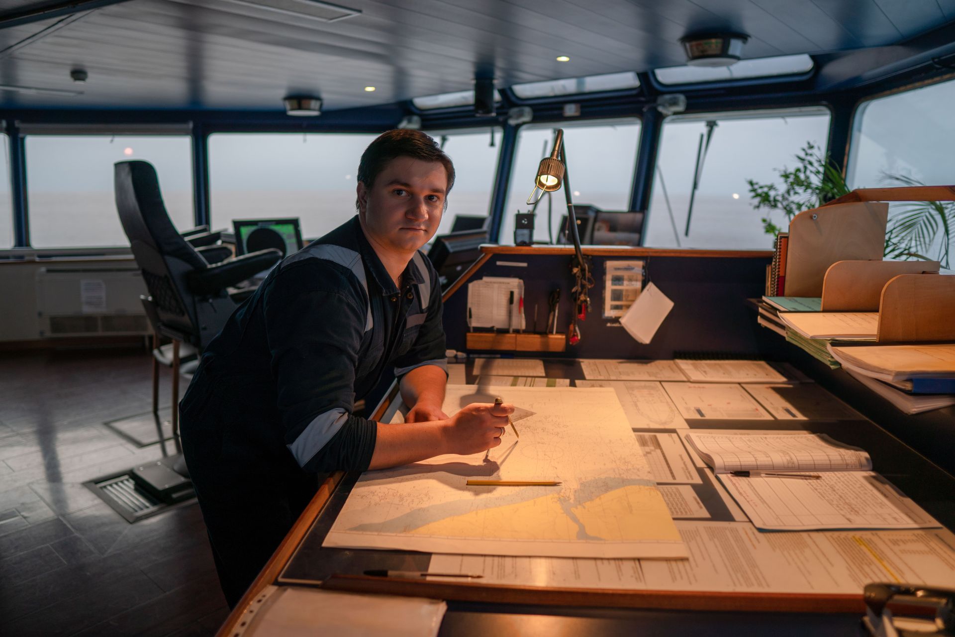 Maritime professional plotting course on navigation chart in ship's bridge at dusk