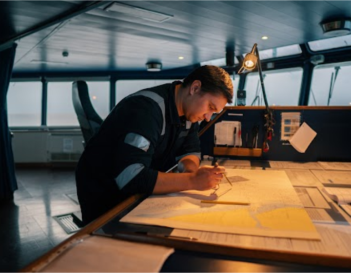 A young officer aboard a ship meticulously plotting a course on a navigational chart in a well-lit bridge, illustrating traditional maritime navigation.