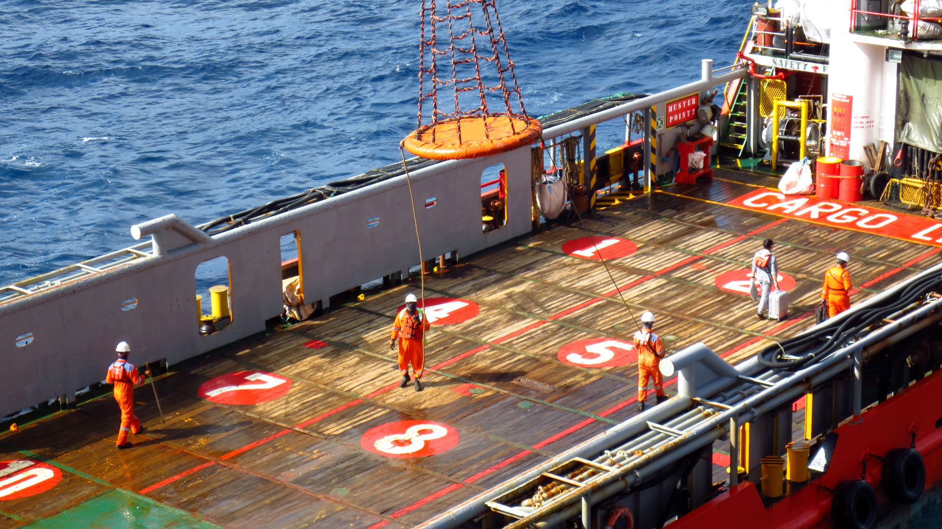 Seafarers working on a ship deck, cargo operations underway with safety gear visible, emphasizing maritime labor and safety standards.