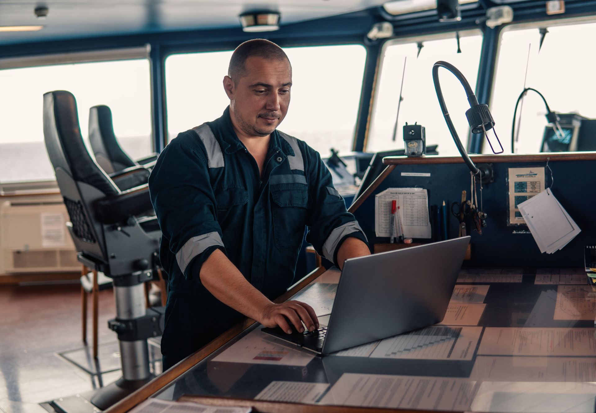 Maritime officer working on a laptop in the ship's bridge, organizing logistics with a focus on digital solutions.